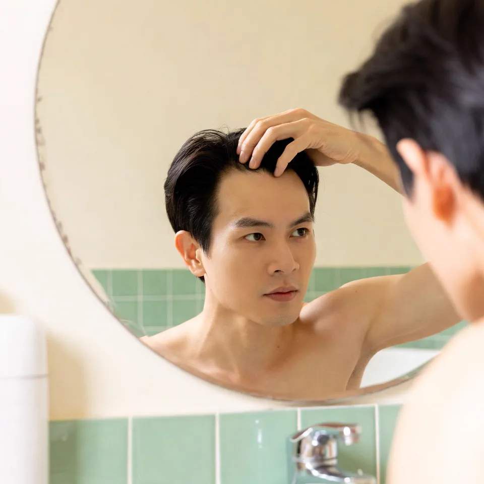 Người dùng kiểm tra da đầu trước gương khi nhận thấy cảm giác bất thường
